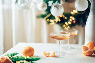 Two glasses of champagne and tangerines on a table against blurred christmas background with...