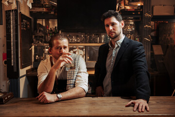 Caucasian barkeeper and male customer standing at bar drinking out of whiskey glass 