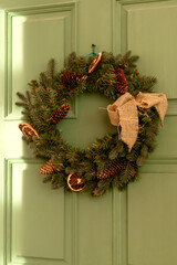 Festive Christmas wreath made of fir branches on a green wooden door.The wreath is decorated with...