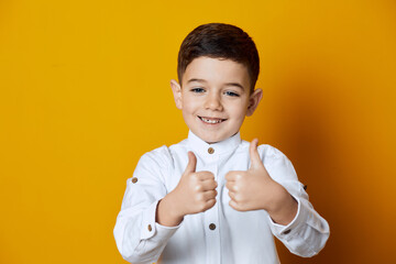Portrait of a kid pointing his thumbs up showing like sign, while wearing white shirt.