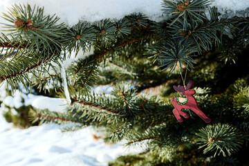 Vintage Christmas tree decoration. Retro red moose toy and icicles on snow-covered tree branches outside in garden.