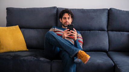 Fototapeta premium Portrait of caucasian man using smartphone sitting on couch at beautiful house