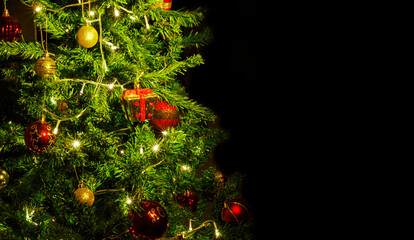 Close up of decorations on a Christmas tree with lights on. Selective focus and black background.