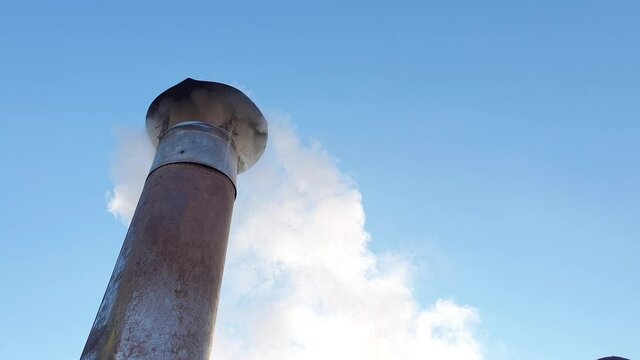 Smoke comes from the chimney of the house. The pipe on the roof. The house with a chimney. Smoke in the blue sky.