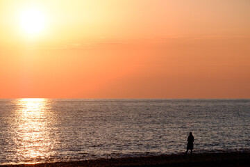 Fototapeta premium minimalism silhouette of a man on the seashore at sunset. orange sky and seashore