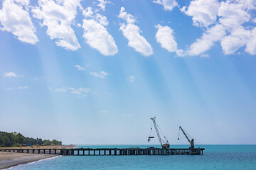 natural phenomenon streaks of light fall through the clouds on a sea pier with installed cranes