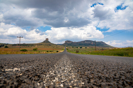 Low angle asphalt tar road in the foreground with a landscape in the Eastern Freestate of South Africa with an empty road and mountains 