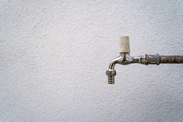 Old faucet for the outside on a long pipe with a white facade in the background