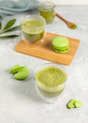 Obraz na płótnie Canvas Two glasses with matcha tea and green macaroon cakes on a gray background. Close-up, vertical