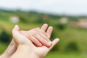 Close up view of unrecognizable couple holding hands on green background. Cropped horizontal view of unrecognizable caucasian people caressing hands. People an emotions concept.