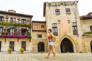 Horizontal view of unrecognizable woman with backpack on holidays looking at the ancient spanish city of Santillana del Mar. Travel and holidays concept in european cities.