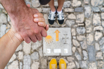Top view of unrecognizable couple holding hands feet at spanish Saint james way. Cropped horizontal view of friends stepping on Saint James pilgrim sign. Travel and people background.