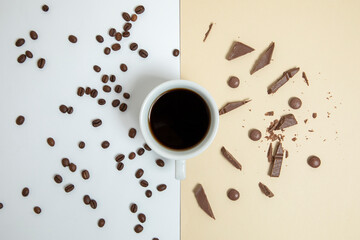 a cup of coffee in the middle with pieces of chocolate and coffee beans. Light brown and white background.
