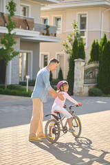 Dad helping his daughter learn riding a bike