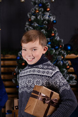 Fototapeta na wymiar portrait of a boy in a sweater in decorated room with christmas tree and presents. dark blue colors.