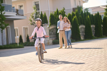 Fototapeta premium A girl riding a bike while her parents watching her