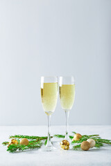 Glasses with sparkling wine type champagne with fir branches and golden Christmas tree decorations on light background