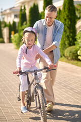 A man supporting a girl while she riding a bike