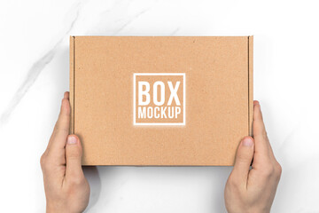 Hands with cardboard box mockup, top view. White table background. Suitable for food, cosmetic or...