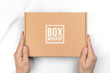 Hands with cardboard box mockup, top view. White table background. Suitable for food, cosmetic or medical packaging. Shipping and delivery concept