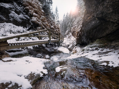Cold early winter mountain forest landscape in Slovakia Tatry mountain. Small creek flowing down and washing the huge boulders on its way. First sun rays lite young snow islands.