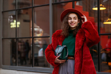 Happy smiling fashionable woman wearing trendy orange faux fur coat, hat, green turtleneck sweater,...