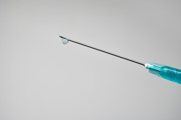Needle of a syringe with a drop of the drug on the tip on a white background