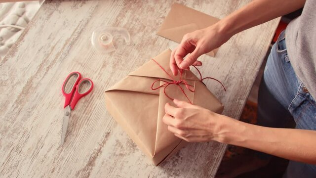 Overhead view of young woman wrapping gift box on table at home. Woman wrapping gift box
