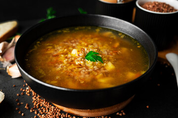 Buckwheat soup on a dark background. Buckwheat soup in a black bowl.