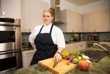 Chef Megan Gill in a kitchen looking at camera with confidence, while having one hand on her culinary knife. 