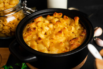 Mac and cheese, american style macaroni pasta in cheesy sauce on dark background.