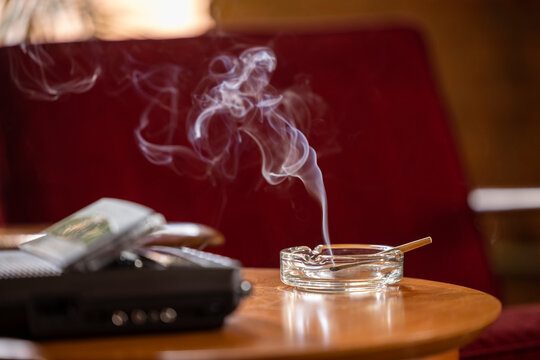 Home Interior, detail of side table with vintage tape recorder / answering machine and ashtray that has a lit CBD pre-roll joint, cigarette with smoke rising