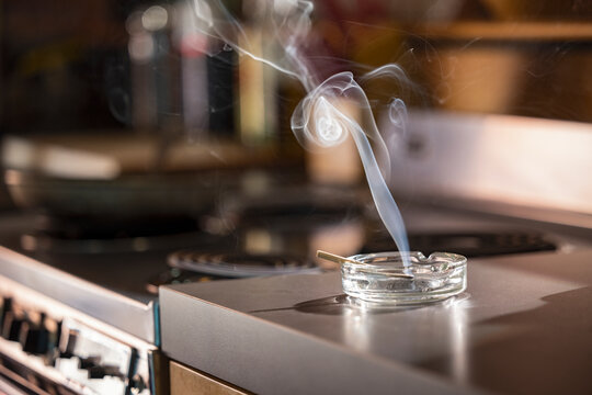 Home Interior, detail of ashtray that has a lit CBD pre-roll joint, cigarette with smoke rising sitting in kitchen next to stove top