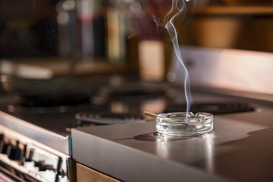 Home Interior, detail of ashtray that has a lit CBD pre-roll joint, cigarette with smoke rising sitting in kitchen next to stove top