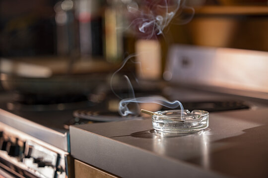 Home Interior, detail of ashtray that has a lit CBD pre-roll joint, cigarette with smoke rising sitting in kitchen next to stove top