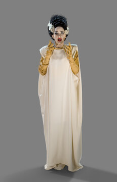 Portrait of a woman in a Bride of Frankenstein Halloween costume looking into camera frightened, against gray background. 