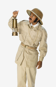 Portrait of a boy dressed up as archaeologist mummy hunter with a fake mustache and sideburns holding a lantern, against a white background