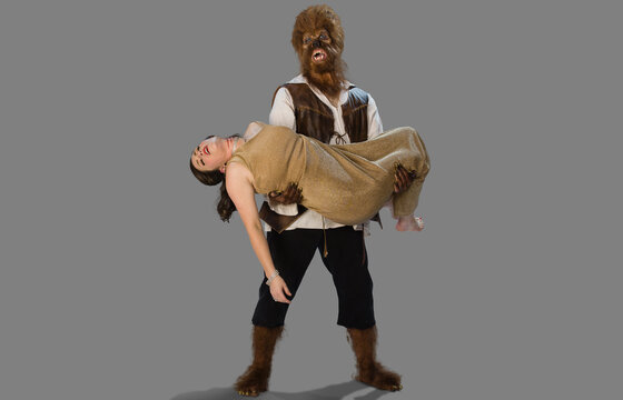 Wolfman werewolf holding a dead woman and lover, in his arms with a distraught and sad expression on his face, two people in Halloween costumes on gray background