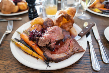 Roast beef on a white plate with roast potatoes and Yorkshire pudding with vegetables in a...