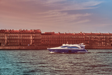 Obraz premium The yacht is sailing on the river in the city . Beautiful boat on the background of architecture . Travel by water .