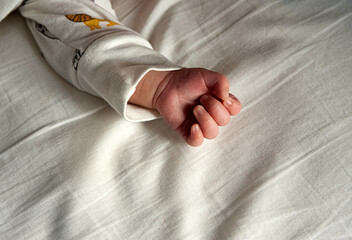 baby in pyjamas closing hand on white sheet