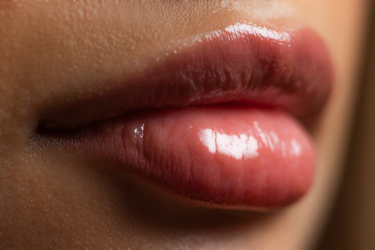Extreme close up of plush lips wearing glossy lipstick.