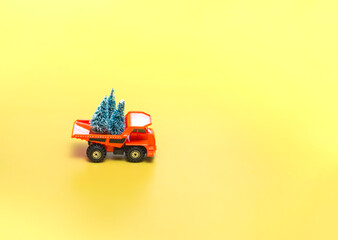 Yellow truck with Christmas trees on a beige background with lights. Holidays concept. Close up, with copy space.