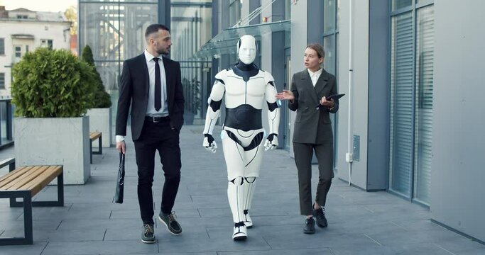 Business man in suit speaking with his female colleague at the street. Woman using tablet computer while managing droid and telling something to her male partner. Innovations and cyber droid concept