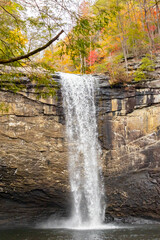 A vertical photograph of a waterfall over a stone cliff in the forest in autumn.