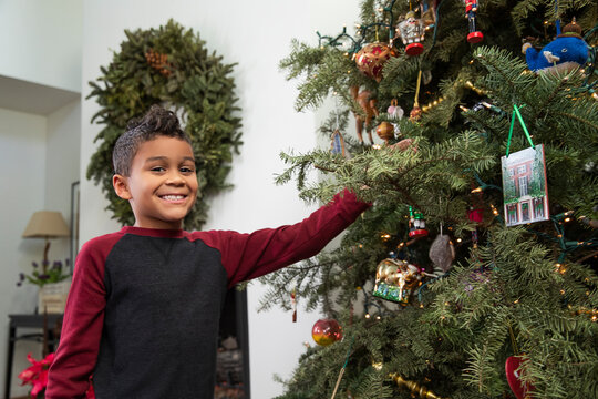 Young boy smiling at camera while decorating Christmas tree.