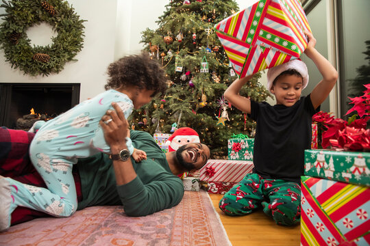 Family wrestling and playing by Christmas tree, opening gifts on Christmas Eve.