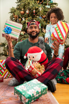 Father holding Christmas gift in each hand, looking into camera with questionable expression.