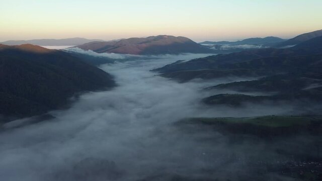 Aerial view on amazing flowing morning fog spreads over green meadows in autumn mountains. Ukrainian Carpathian mountains. UHD 4k video