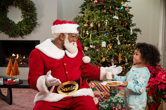 Shy girl handing milk and cookies to Black Santa Claus